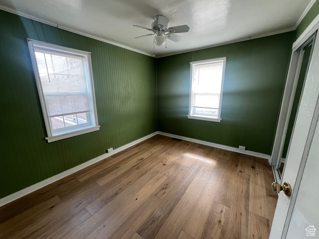 Unfurnished room with crown molding, hardwood / wood-style flooring, ceiling fan, healthy amount of natural light, and baseboards