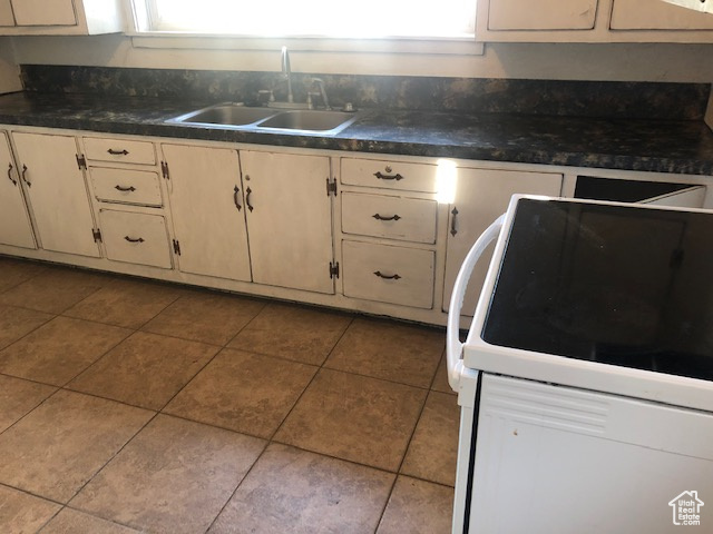 Kitchen featuring white range with electric stovetop, a sink, dark countertops, and tile patterned floors