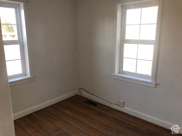 Unfurnished room with dark wood finished floors, baseboards, and healthy amount of natural light