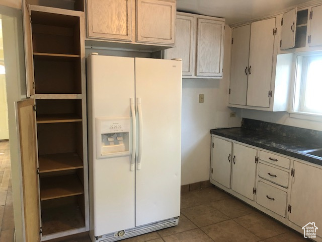 Kitchen with white fridge with ice dispenser, open shelves, dark countertops, tile patterned flooring, and baseboards
