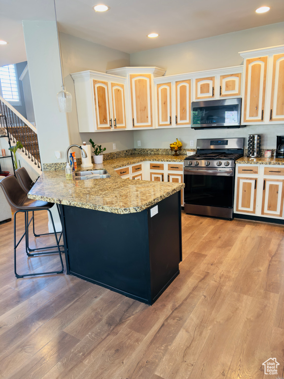 Kitchen with stainless steel appliances, a sink, a peninsula, light brown cabinetry, and recessed lighting