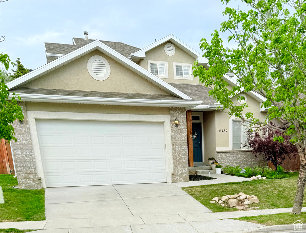 Traditional-style home with stucco siding, a shingled roof, driveway, and brick siding