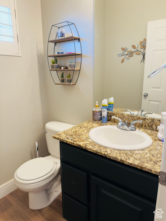 Half bathroom featuring wood finished floors, vanity, toilet, and baseboards