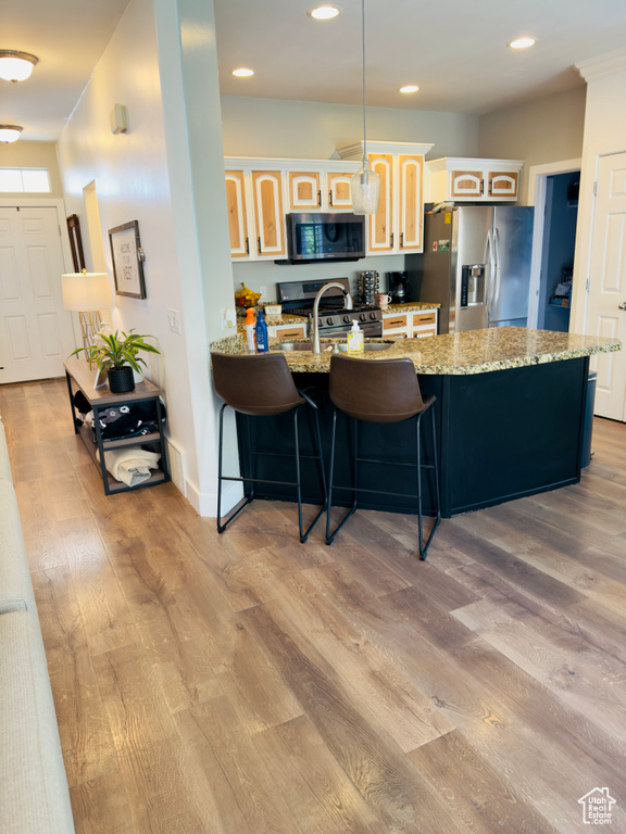 Kitchen featuring appliances with stainless steel finishes, a peninsula, light wood-type flooring, a breakfast bar, and glass insert cabinets