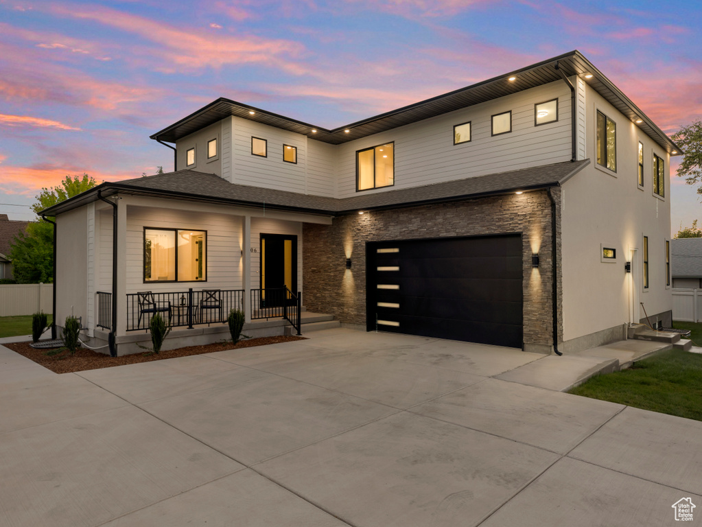 Modern home featuring covered porch, a garage, driveway, and stone siding