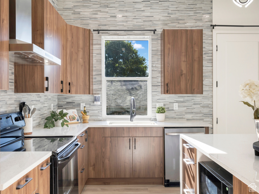 Kitchen featuring wall chimney range hood, black / electric stove, a sink, backsplash, and light countertops