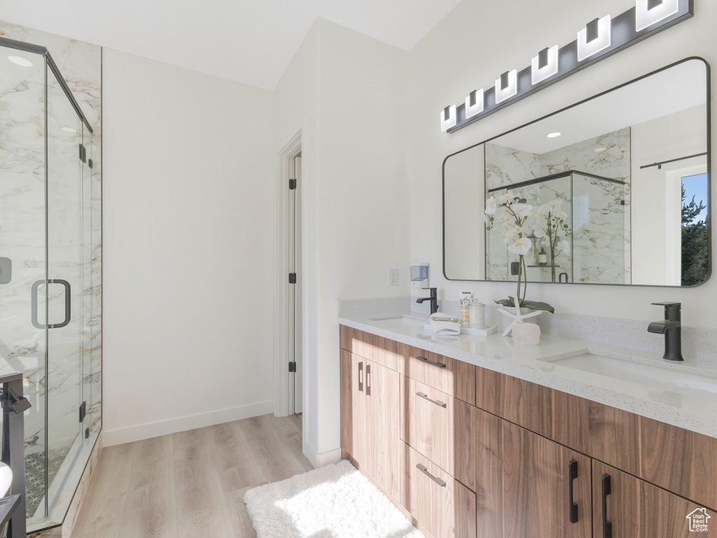 Full bath featuring wood finished floors, a marble finish shower, and double vanity