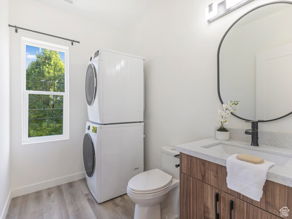 Bathroom with stacked washer / drying machine, wood finished floors, toilet, vanity, and baseboards