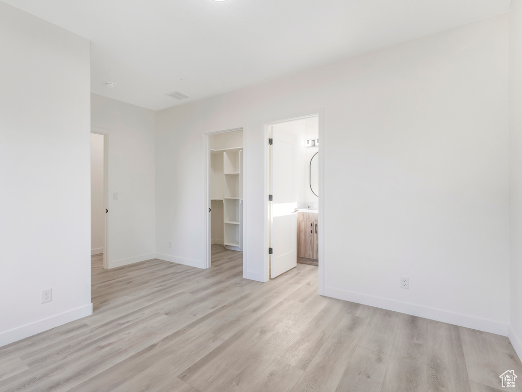 Unfurnished bedroom featuring light wood-type flooring, a walk in closet, baseboards, a closet, and ensuite bathroom