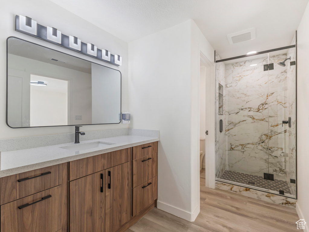 Full bath featuring wood finished floors, baseboards, a marble finish shower, and vanity