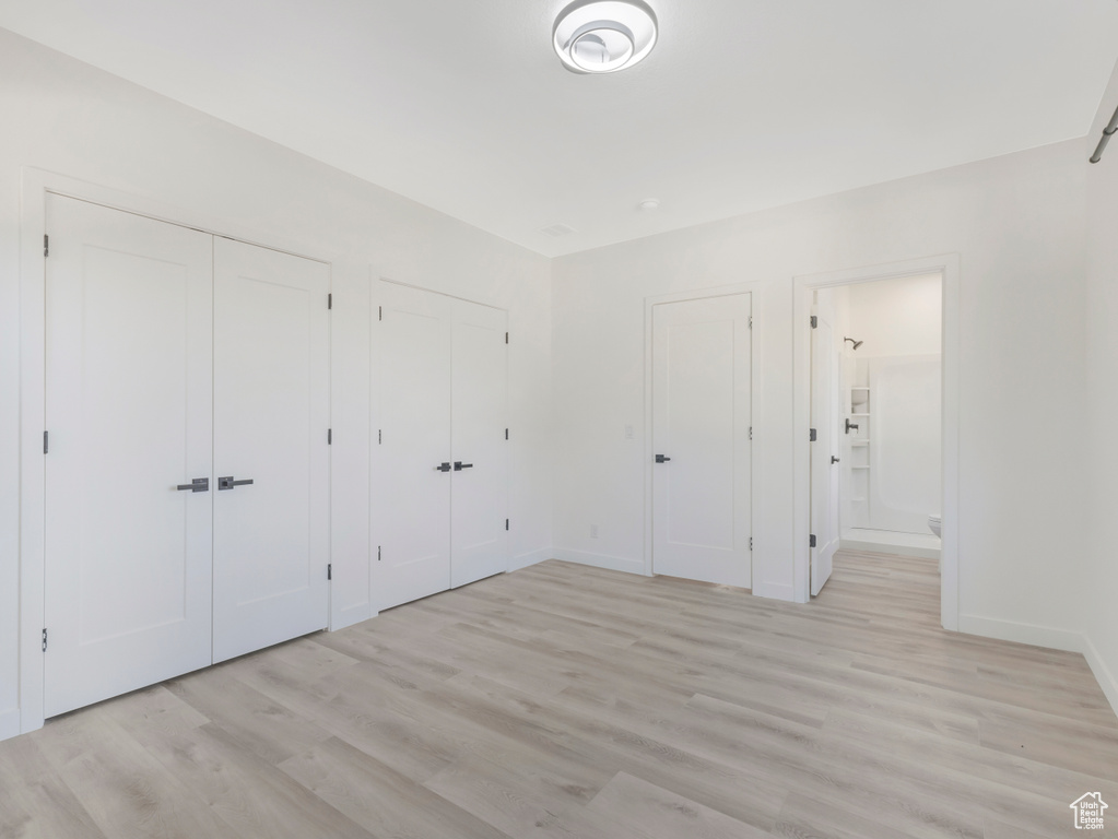 Unfurnished bedroom with two closets, light wood-type flooring, baseboards, and ensuite bathroom