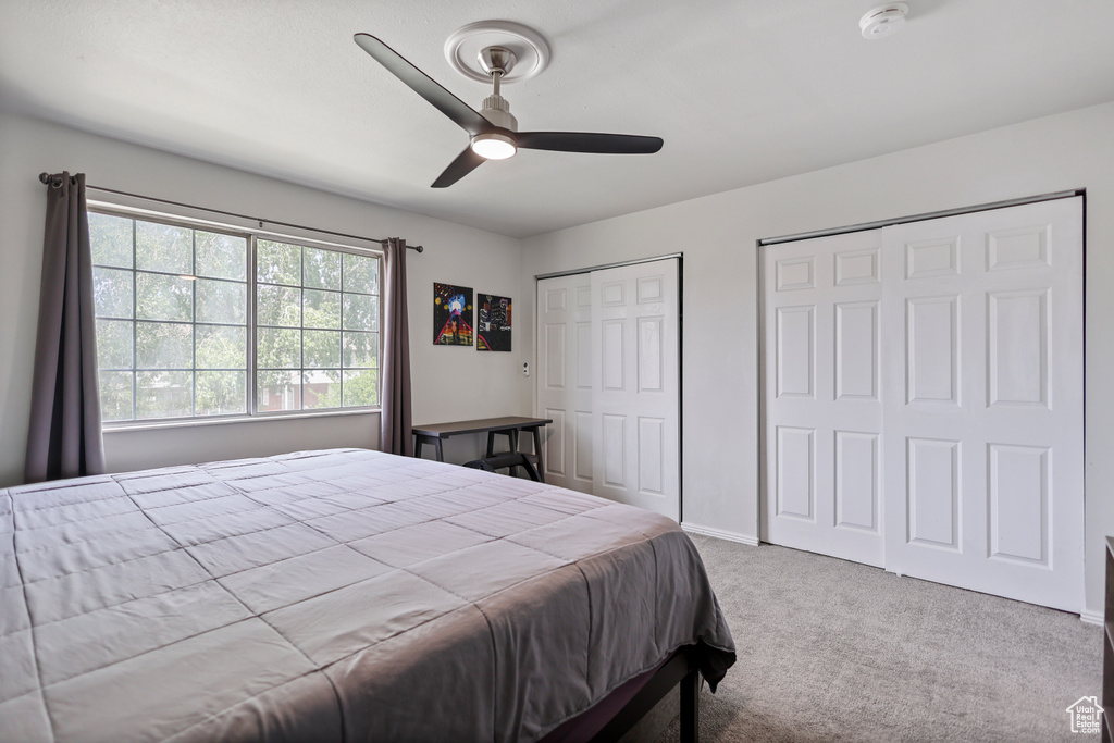 Carpeted bedroom featuring multiple closets, a ceiling fan, and baseboards
