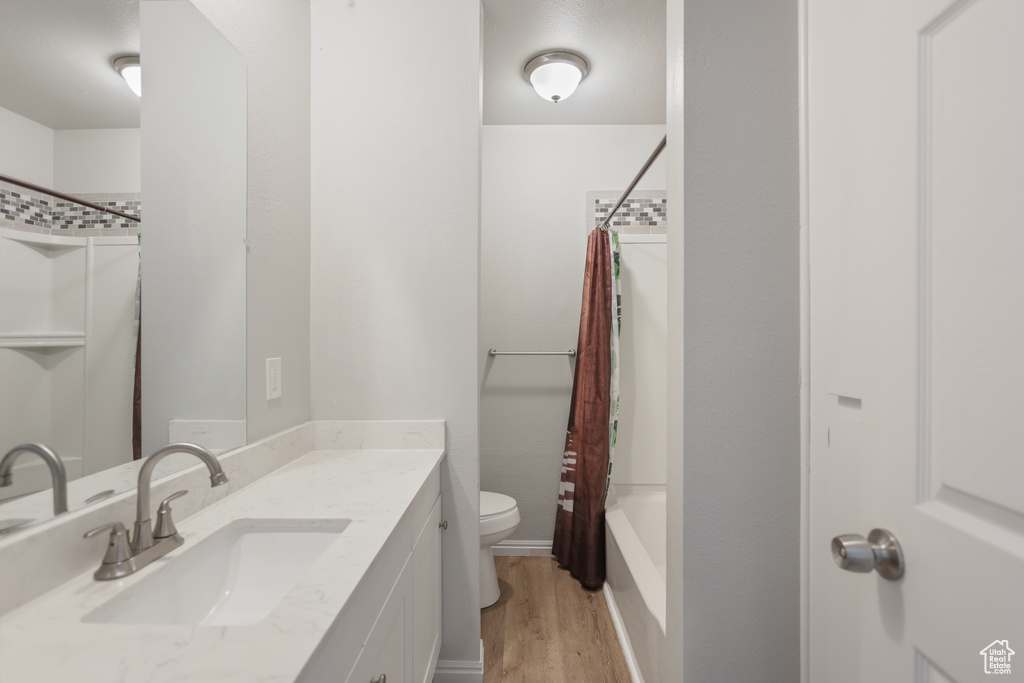 Bathroom featuring toilet, wood finished floors, vanity, and shower / bath combination with curtain
