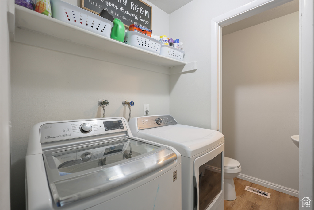 Clothes washing area featuring separate washer and dryer, light wood-type flooring, and baseboards
