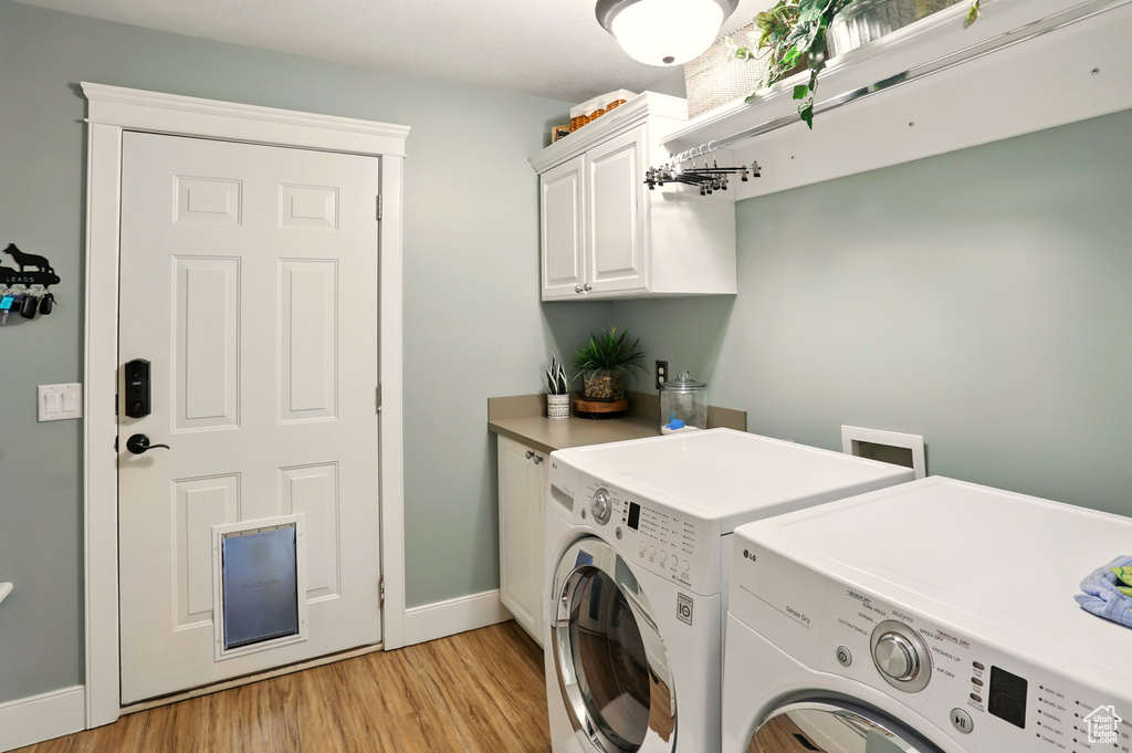 Laundry area featuring washing machine and clothes dryer, cabinet space, light wood finished floors, and baseboards