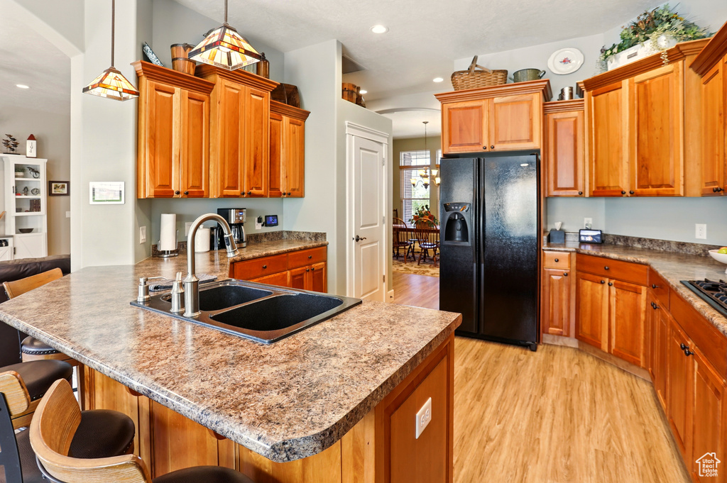 Kitchen featuring black fridge with ice dispenser, a sink, light wood-style floors, a peninsula, and a kitchen bar