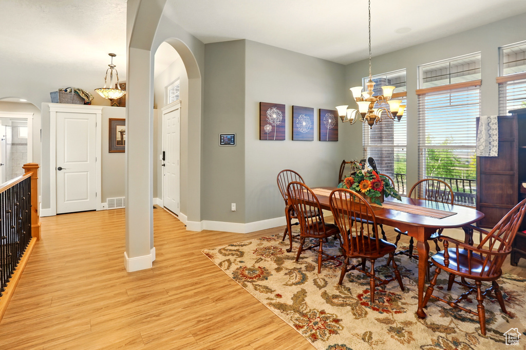 Dining area with arched walkways, light wood finished floors, a chandelier, and baseboards
