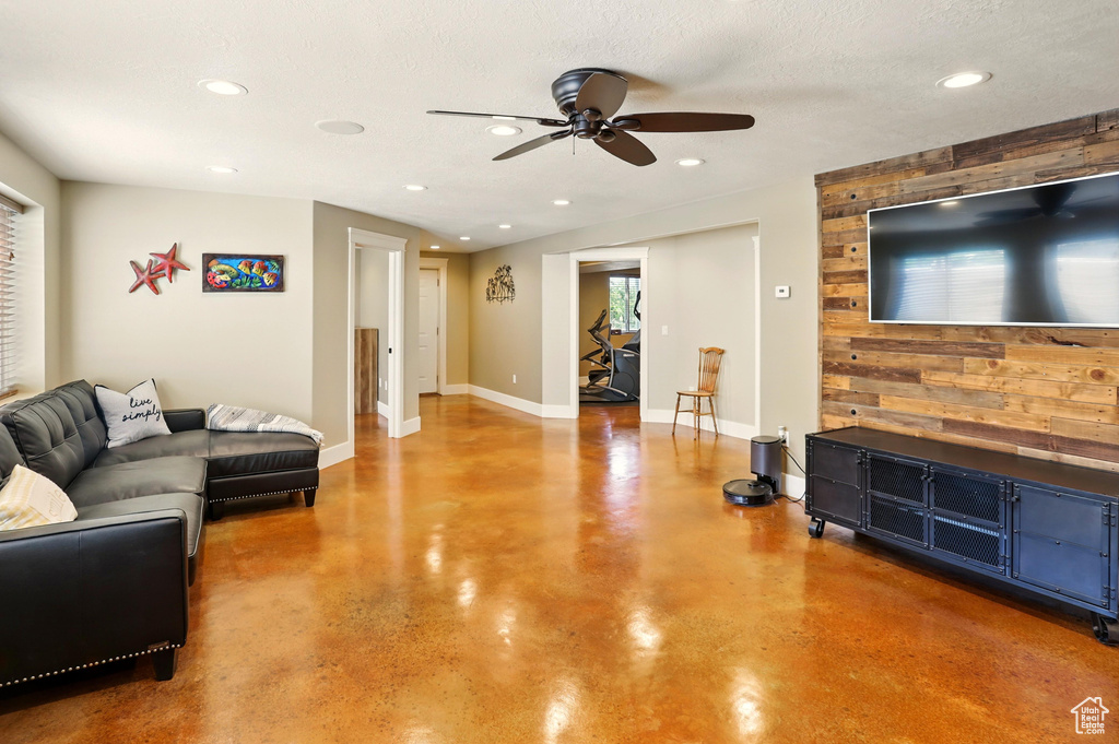 Living area with concrete flooring, a ceiling fan, recessed lighting, wooden walls, and baseboards