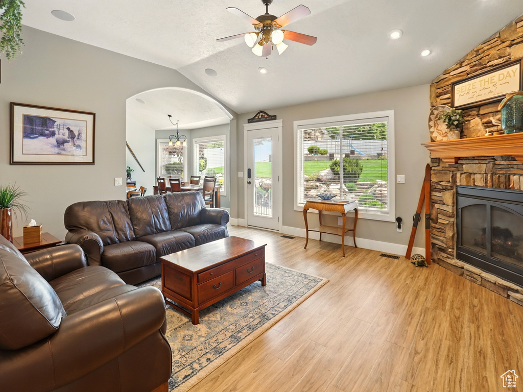 Living room featuring vaulted ceiling, arched walkways, a stone fireplace, a ceiling fan, and light wood-type flooring