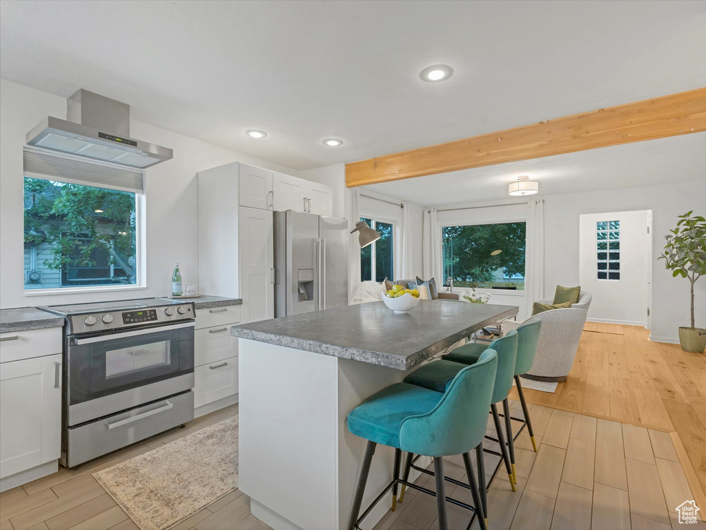 Kitchen featuring appliances with stainless steel finishes, wall chimney exhaust hood, a breakfast bar area, light wood-type flooring, and a center island