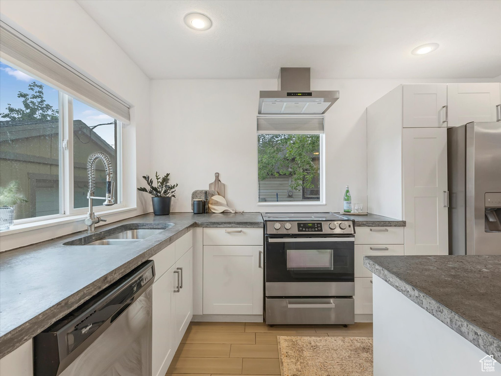 Kitchen with stainless steel appliances, wall chimney exhaust hood, a sink, light wood-style floors, and white cabinets