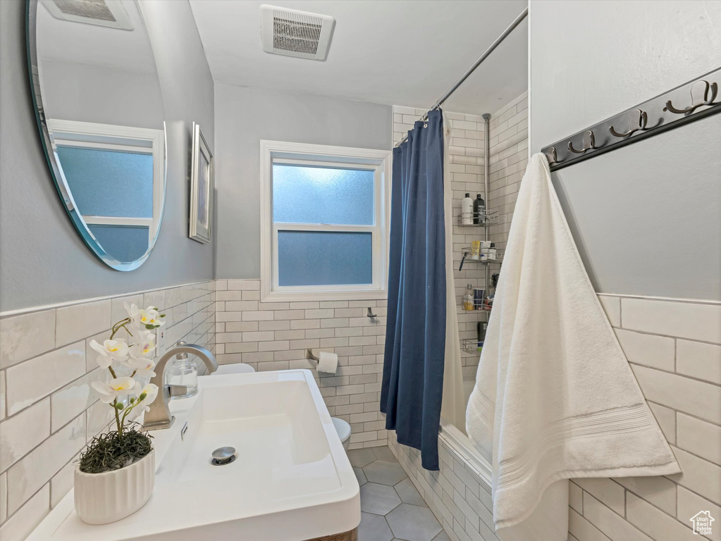 Full bath featuring tile walls, tile patterned floors, curtained shower, and wainscoting