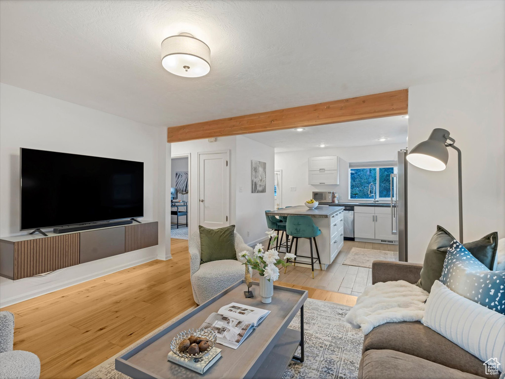 Living area featuring light wood-style floors, beam ceiling, recessed lighting, and baseboards