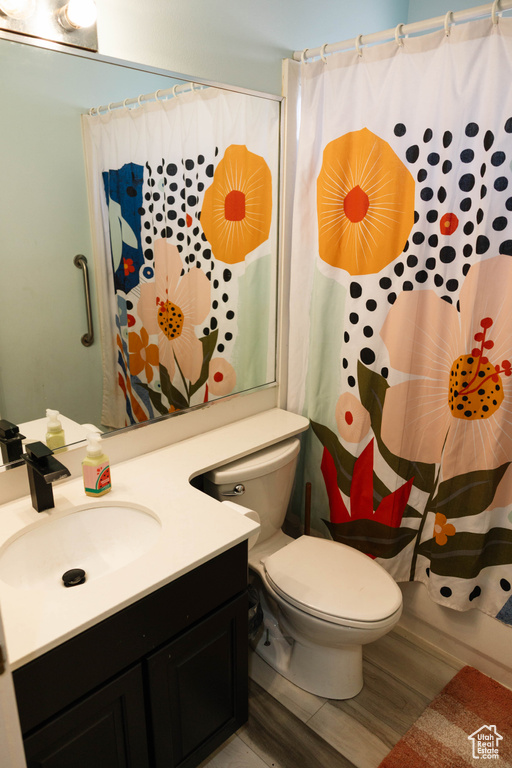 Full bathroom with toilet, vanity, wood finished floors, and curtained shower