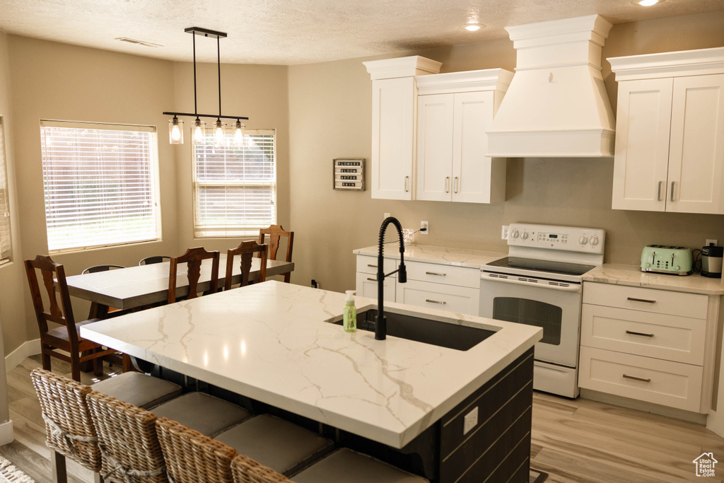 Kitchen with white range with electric stovetop, custom exhaust hood, a sink, light wood-style floors, and white cabinetry