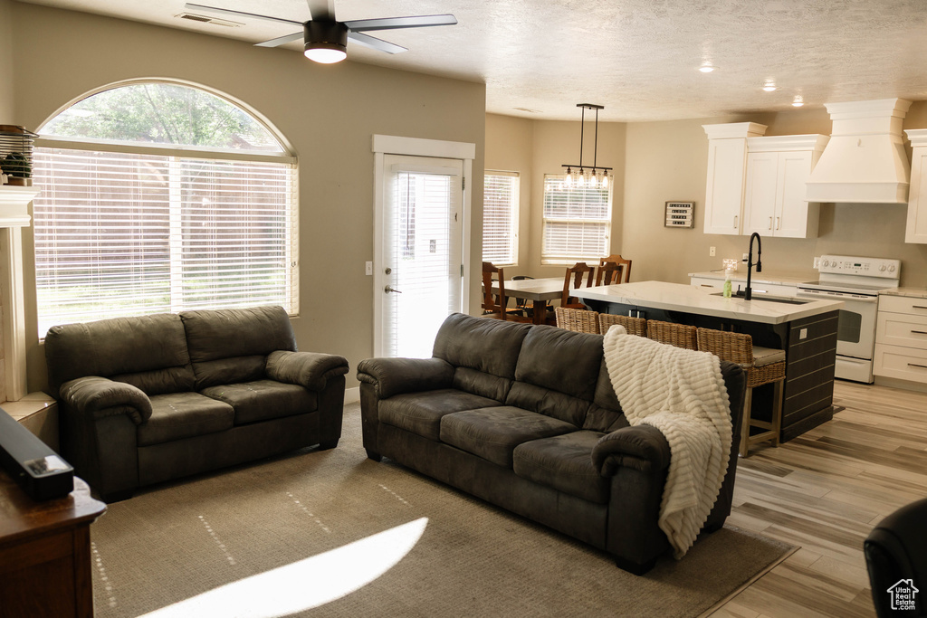 Living room with a ceiling fan, light wood-style floors, a textured ceiling, and a chandelier