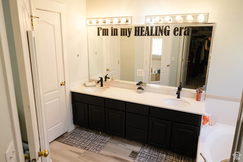 Bathroom with double vanity, a bathtub, and wood finished floors