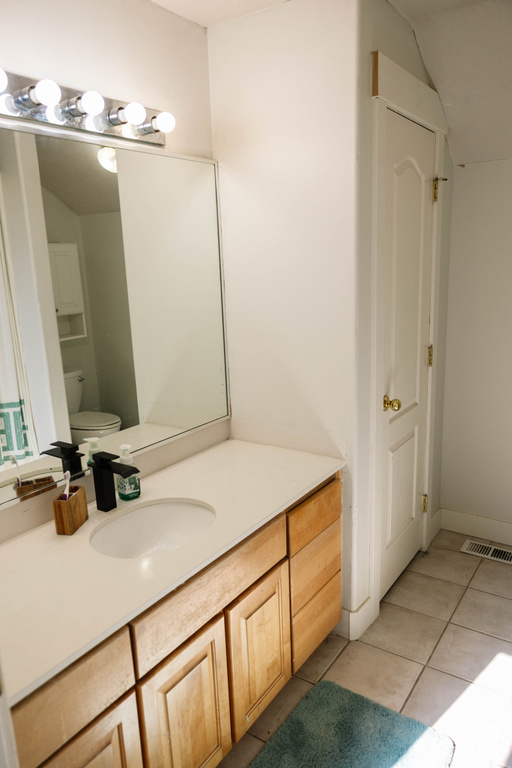 Bathroom featuring tile patterned flooring, toilet, vanity, and vaulted ceiling