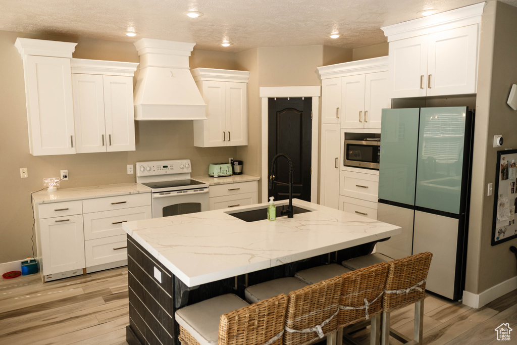 Kitchen with white range with electric stovetop, freestanding refrigerator, a sink, custom exhaust hood, and light wood-type flooring