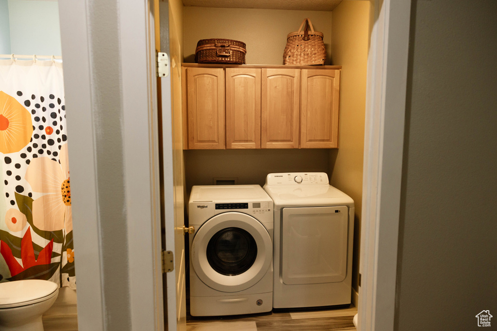 Laundry area with independent washer and dryer, cabinet space, and wood finished floors