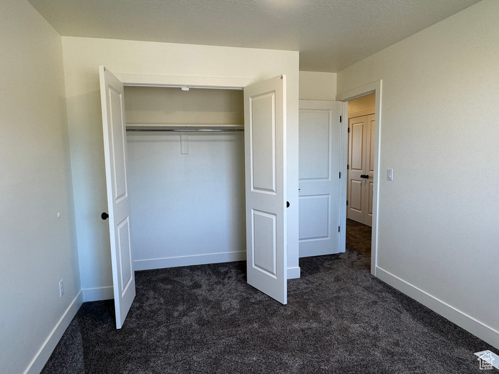 Unfurnished bedroom featuring dark carpet, baseboards, and a closet