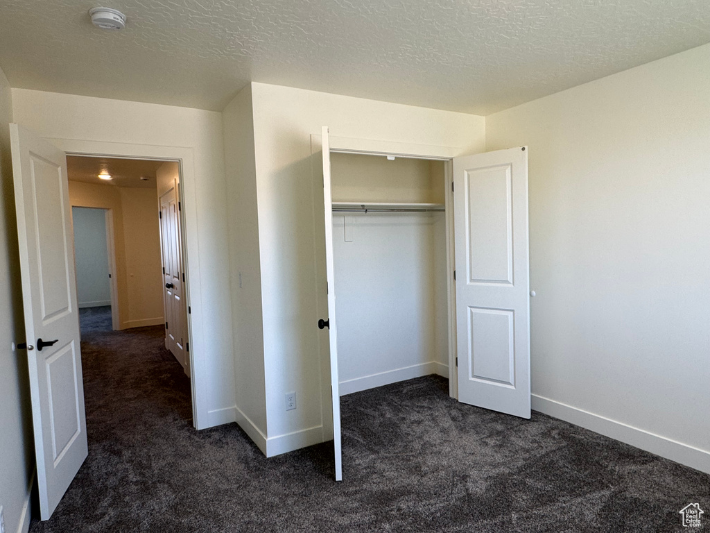 Unfurnished bedroom featuring dark colored carpet, baseboards, a closet, and a textured ceiling