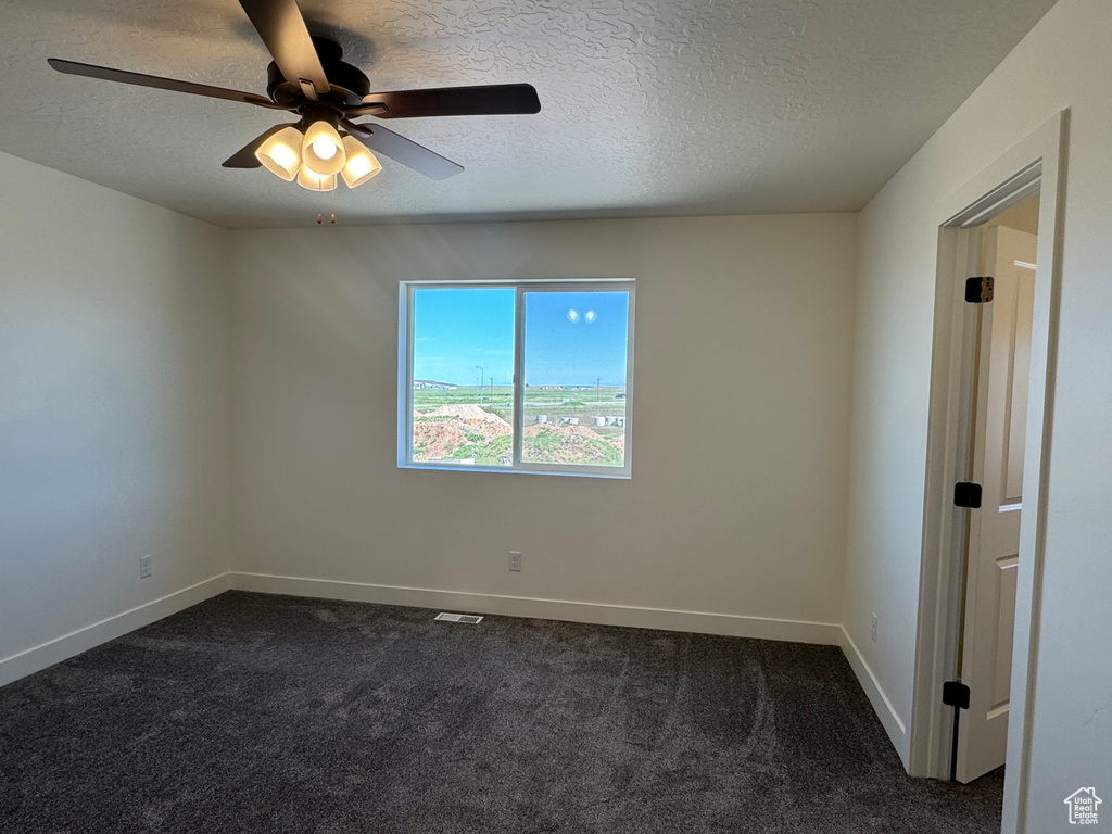 Unfurnished room featuring a textured ceiling, ceiling fan, dark carpet, and baseboards
