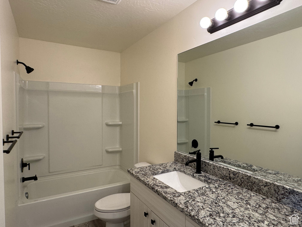 Bathroom with toilet, vanity, washtub / shower combination, and a textured ceiling