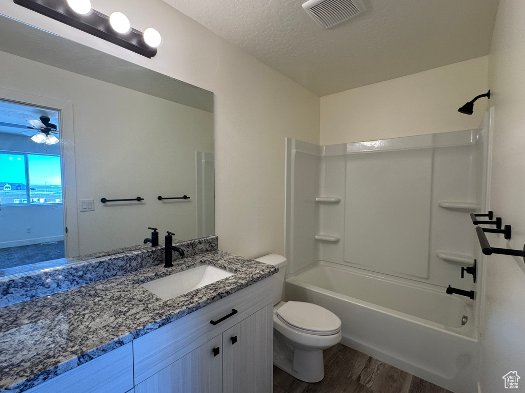 Bathroom with wood finished floors, toilet, vanity, shower / washtub combination, and a ceiling fan