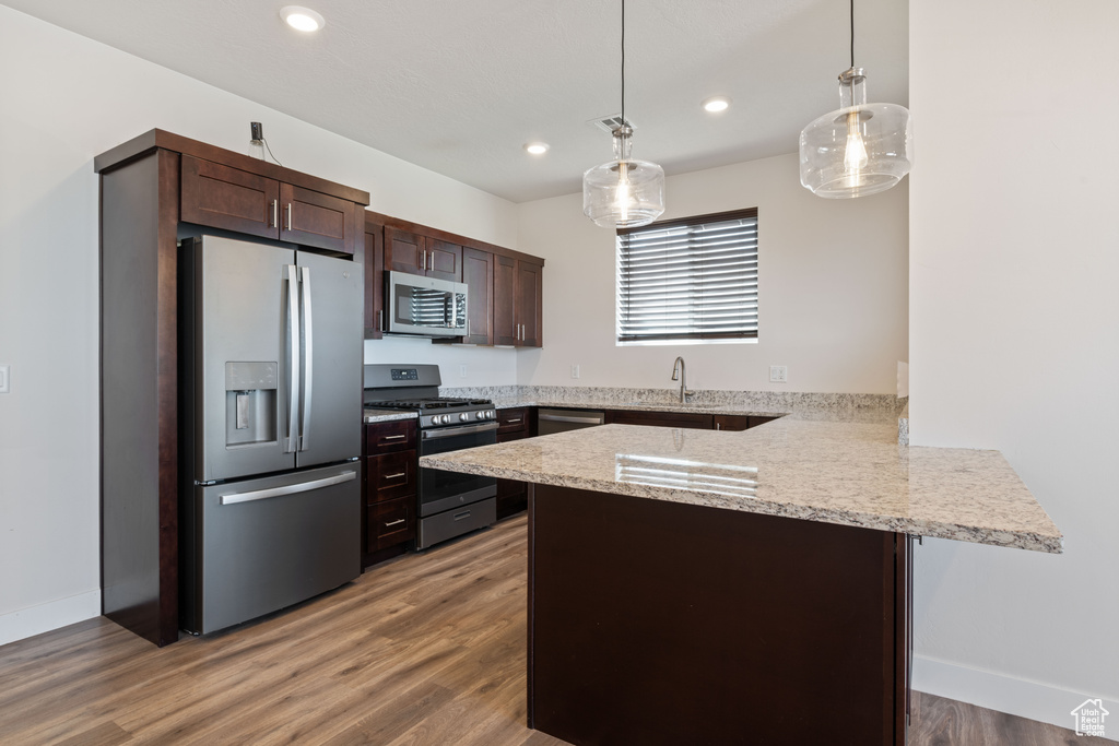 Kitchen featuring stainless steel appliances, a peninsula, dark brown cabinetry, hanging light fixtures, and recessed lighting