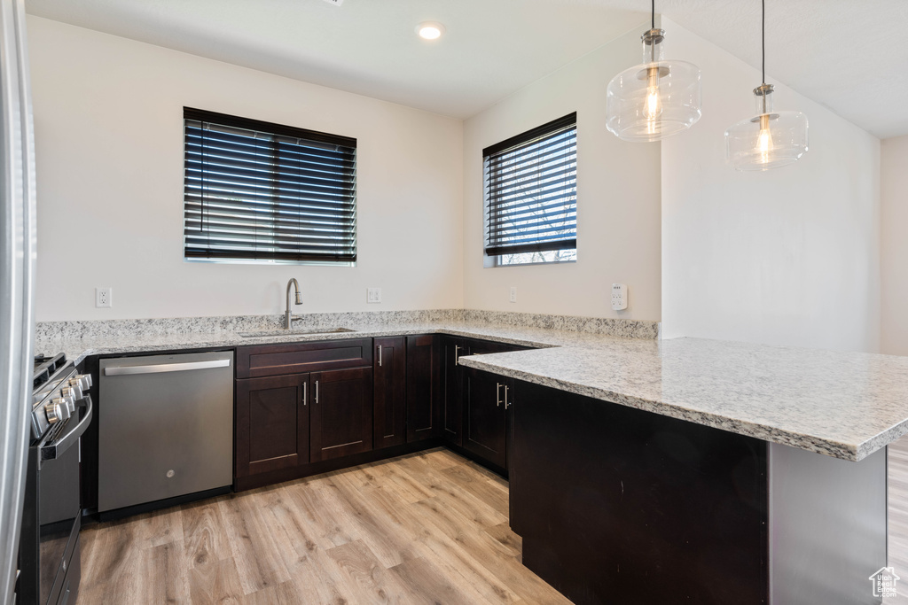 Kitchen featuring appliances with stainless steel finishes, a sink, light wood-type flooring, a peninsula, and pendant lighting