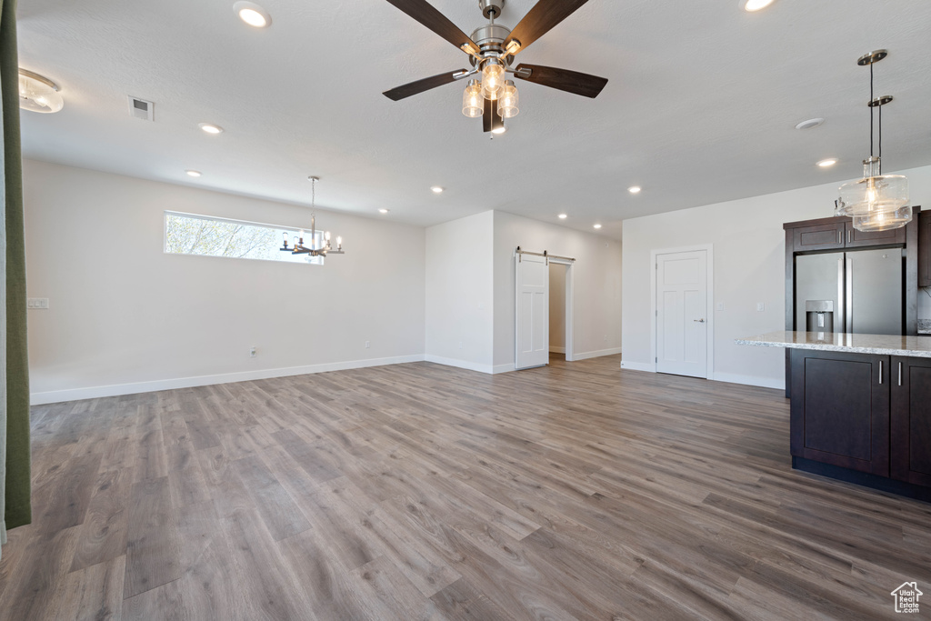 Unfurnished living room with a barn door, recessed lighting, wood finished floors, ceiling fan, and baseboards