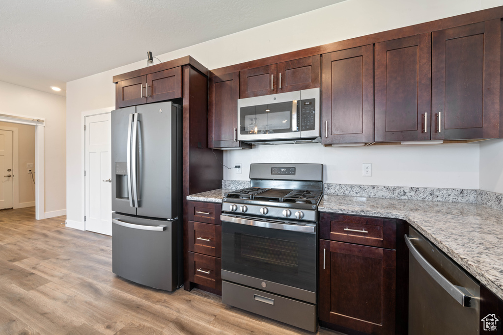 Kitchen featuring appliances with stainless steel finishes, light wood-type flooring, light stone countertops, dark brown cabinetry, and recessed lighting