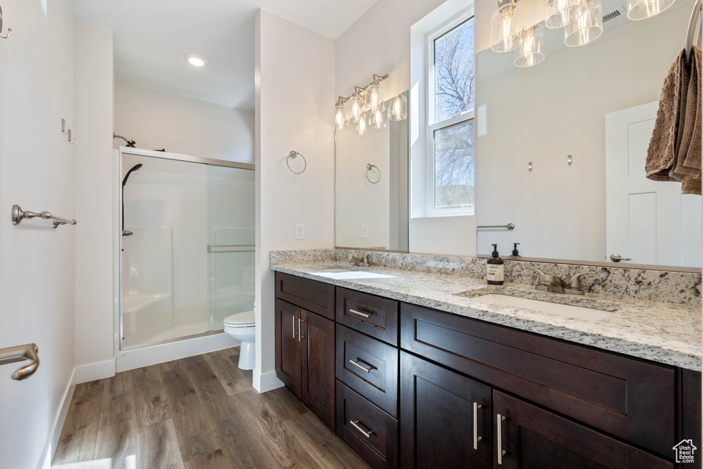 Bathroom featuring wood finished floors, a shower stall, toilet, double vanity, and baseboards