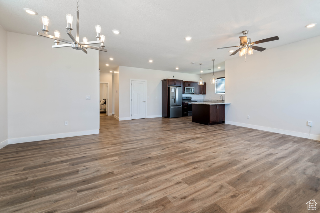 Unfurnished living room with recessed lighting, ceiling fan, wood finished floors, a chandelier, and baseboards