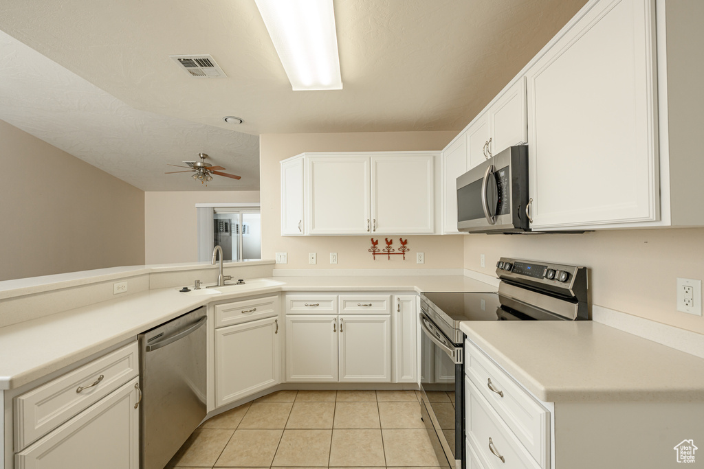 Kitchen with appliances with stainless steel finishes, a sink, light tile patterned flooring, white cabinetry, and ceiling fan