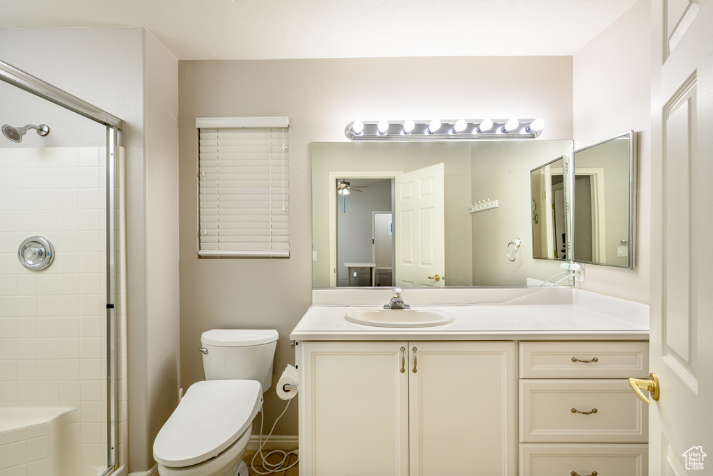 Bathroom with a tile shower, toilet, vanity, and a ceiling fan