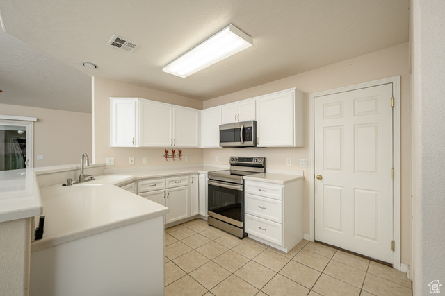 Kitchen featuring appliances with stainless steel finishes, a peninsula, a sink, light tile patterned flooring, and white cabinets
