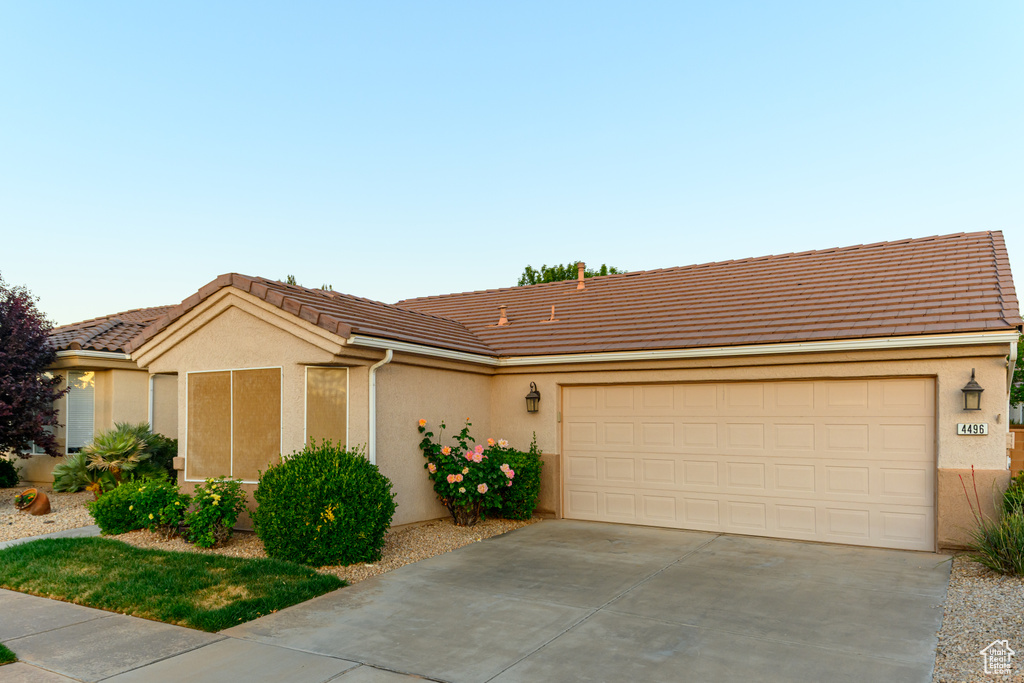 Ranch-style house featuring driveway, a tile roof, an attached garage, and stucco siding