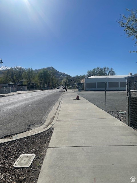 View of asphalt road with sidewalks, a mountain view, and street lights